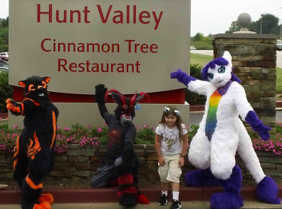 Fursuiters and girl pose in front of a hotel sign