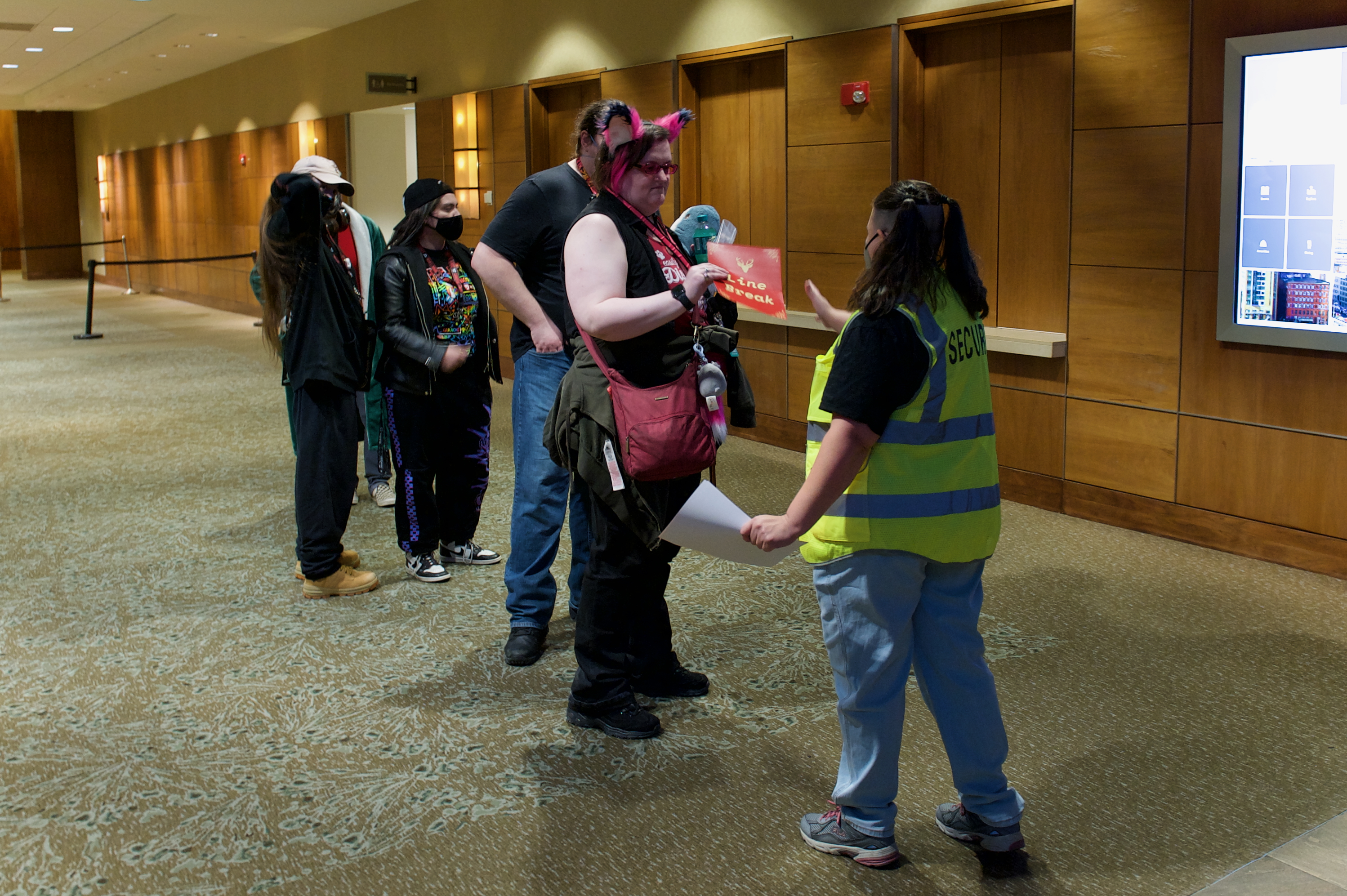 A woman in a high-viz vest instructs people in a line.