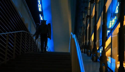 A silhouette of a winged fursuit descends a flight of stairs.